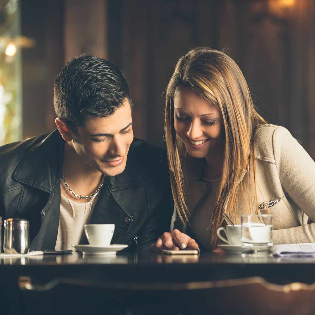 A couple using a phone together at a cafe.